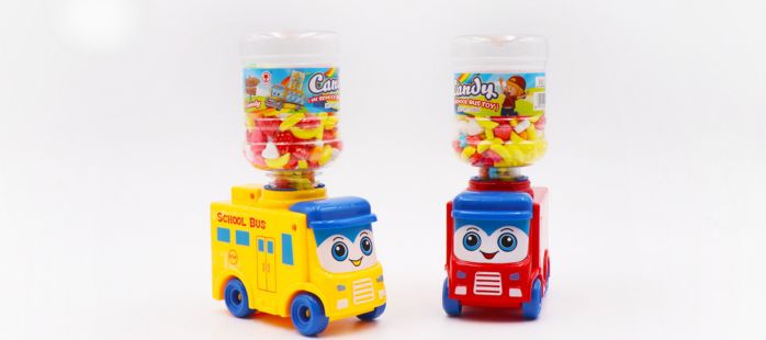 Display of colorful school bus-shaped candy toys with smiling faces. Packaging features a playful design, including a cartoon child and school bus. Clear containers filled with assorted pressed candies are positioned above each toy bus.